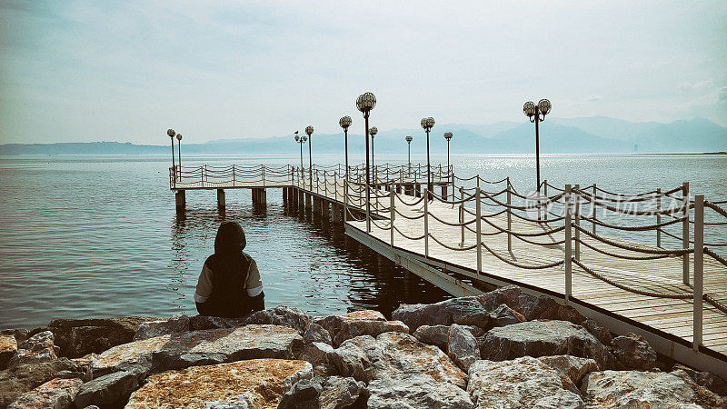 孤独的男孩坐在海边的码头