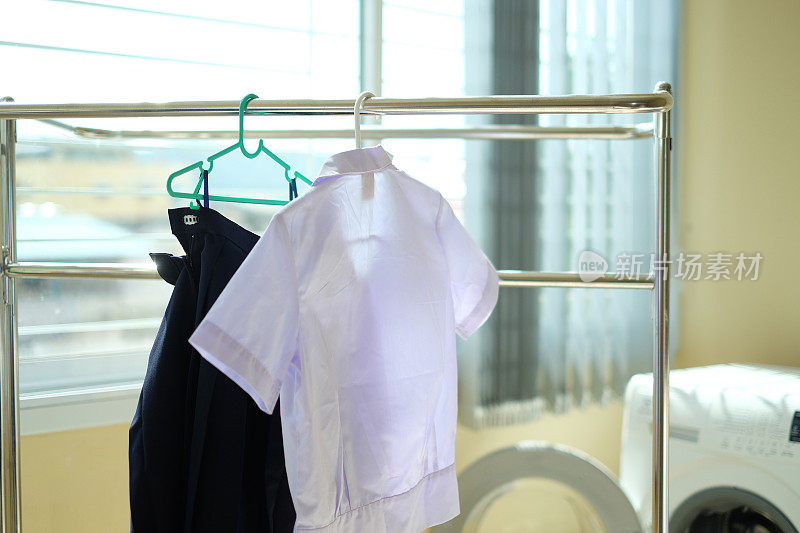 学生洗完的校服挂在晾衣绳上。白衬衫和蓝裙子晾在房子里的衣架上。回到学校的概念。