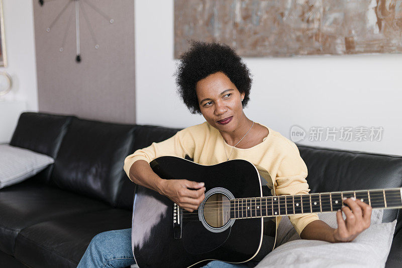 成熟美丽的黑人女性坐在家里的沙发上弹着原声吉他，微笑着，欣喜不已