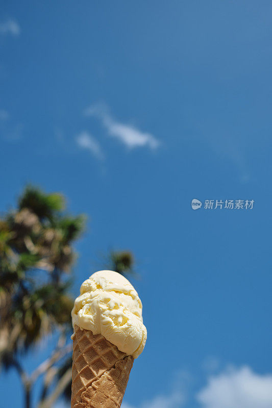 6月一个阳光明媚的日子，在康沃尔的纽基，一只手拿着香草冰淇淋蛋卷，对着晴朗的蓝天。