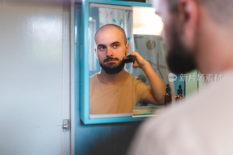 一个年轻秃顶男子在镜子前修剪胡子的特写