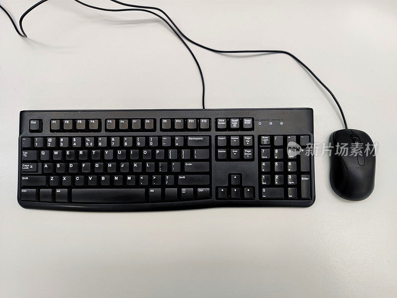 白色办公桌上的无品牌黑色QWERTY键盘，无品牌黑色鼠标和电缆