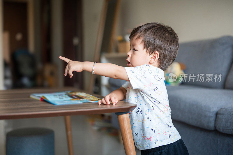 小男孩站在家里客厅的咖啡桌旁看一本书