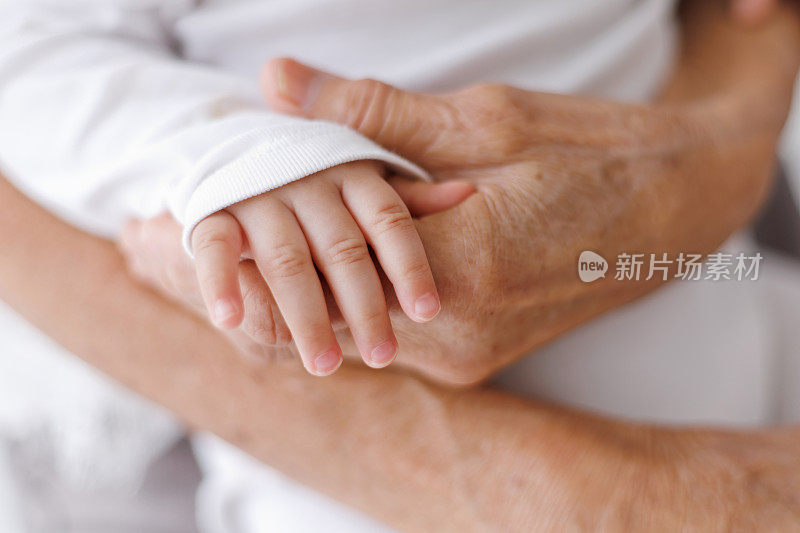 一位年长妇女的手紧紧握住一个女婴的手