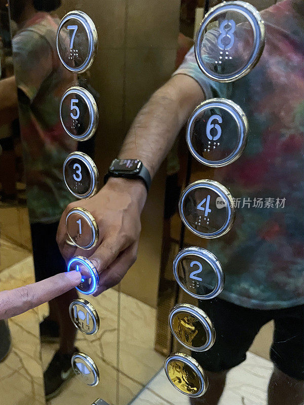 无法辨认的人用食指按电梯键盘上的大厅按钮的图像，反射在闪亮的不锈钢电梯控制面板上，盲文数字，焦点在前景