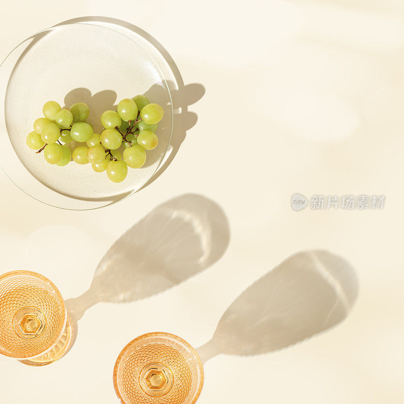 桌上放着两杯白葡萄酒和绿葡萄，最小限度的夏日派对，阳光下的阴影，彩色背景上的现代彩色眼镜，模糊的眩光，复制空间，俯视图