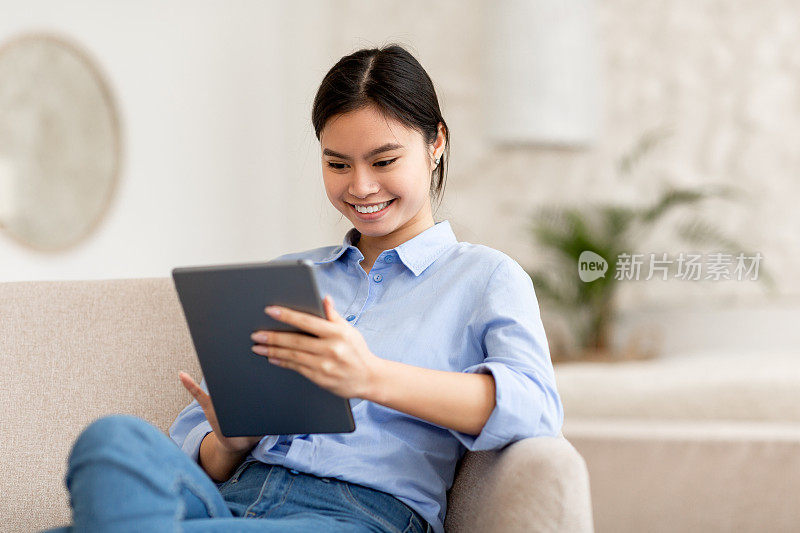 微笑的女士坐在沙发上，使用数码平板电脑
