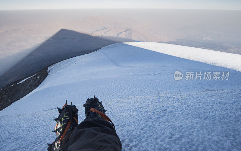 从阿拉拉特山顶看，黎明时分山的锥形阴影，登山者的腿在山顶上踩着冰爪