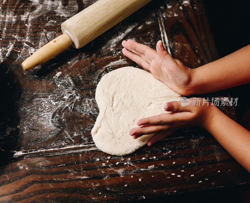 孩子的手在烘烤或在家做饭时在披萨面团上做心形