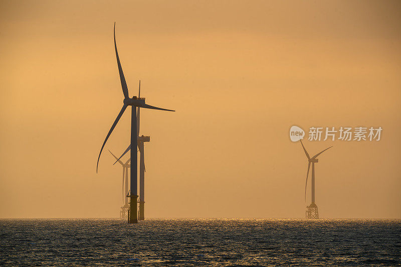 风力涡轮机的风扇在波光粼粼的海面上旋转。