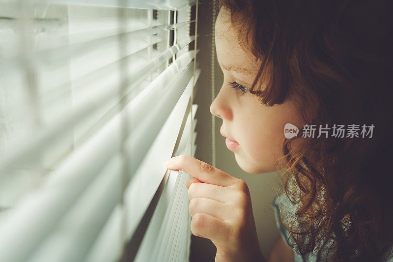 小孩子透过百叶窗望着窗外
