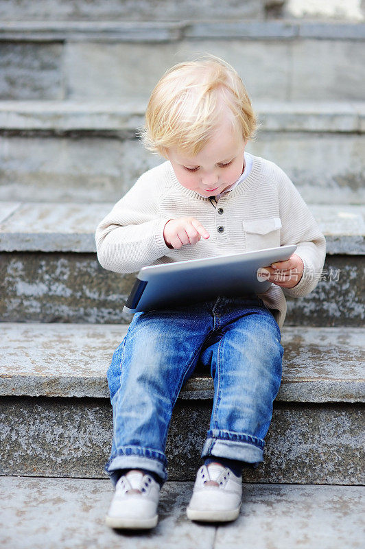 可爱的金发小男孩在户外玩数码平板电脑