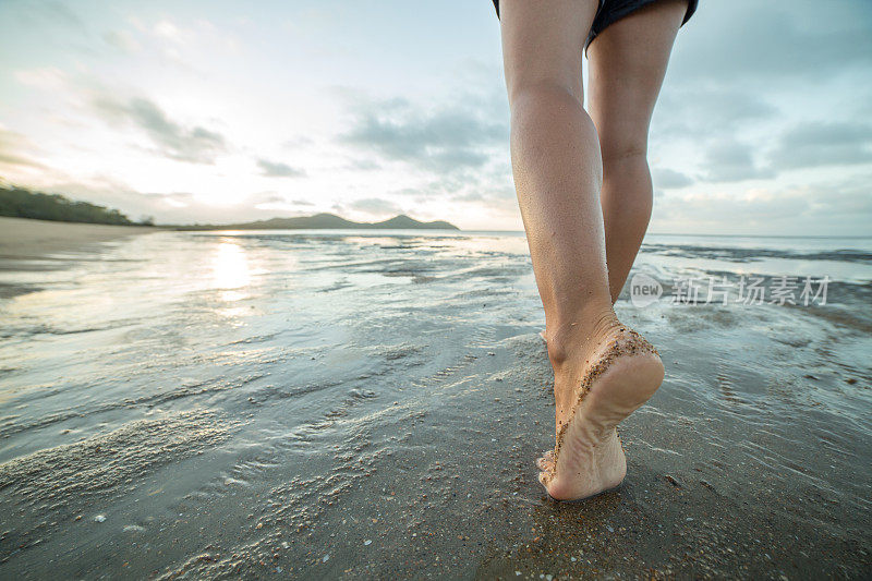在太阳升起时赤脚在海滩上行走的特写