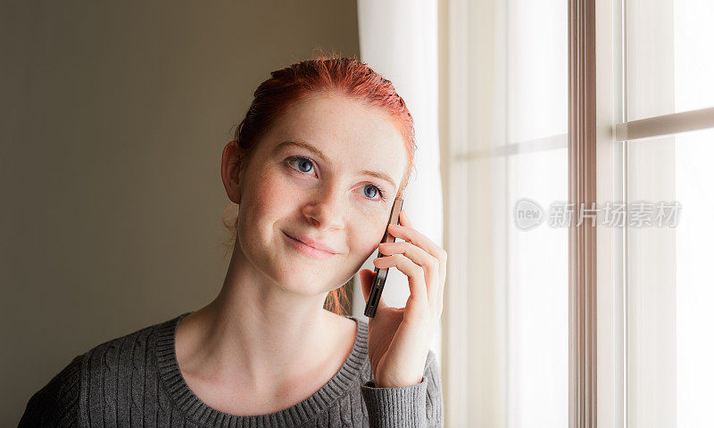 年轻的红发女人在窗口打电话