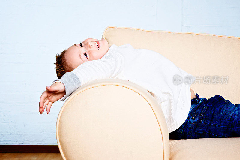 精力充沛的小男孩愉快地伸展在沙发扶手上
