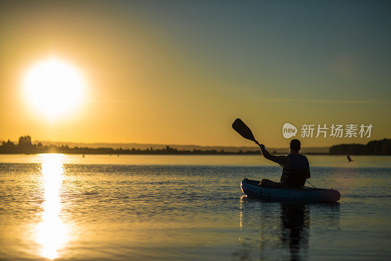 日落时分，一名成年男子在宁静的湖面上划皮艇