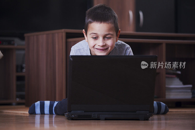 可爱的男孩看着笔记本电脑和笑