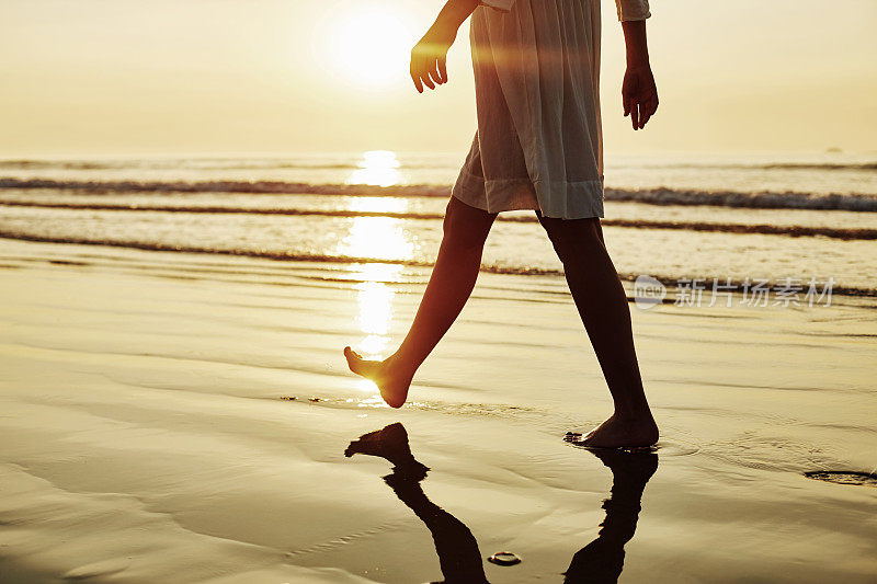 日落时分，穿着太阳裙的女人赤脚走在岸边