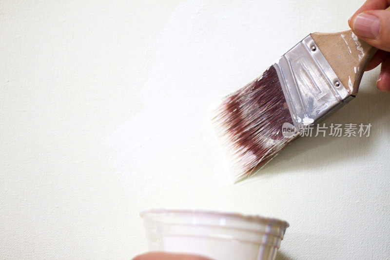 手用油漆刷蘸湿白色油漆，油漆杯