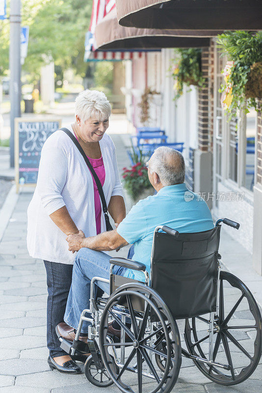 一对老年夫妇在城市人行道上，一个坐轮椅的男人。
