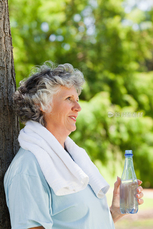 一个女人拿着一瓶水靠在树上休息
