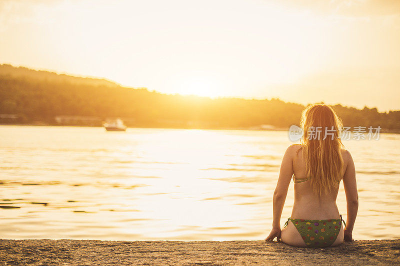 年轻女子坐在码头上欣赏美丽的日落
