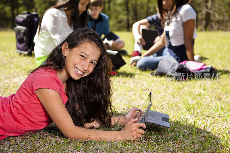 科技:拉丁少女数字平板电脑。朋友的背景。公园