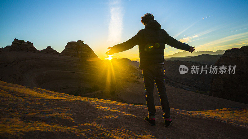 这位年轻的潮人、旅行者和徒步旅行者在犹他州精致拱门附近的红色峡谷里欣赏日出