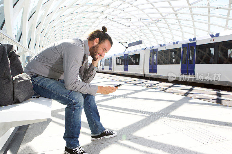 微笑的男人坐在站台上拿着手机