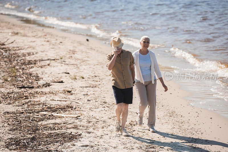 幸福的老年夫妇手牵着手走在河边的沙滩上