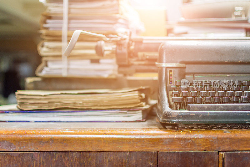 打字机古董古董风格与旧文件或旧信的作家在木制书桌上缩放前视图的打字机，作家或编辑在古董办公室的概念。