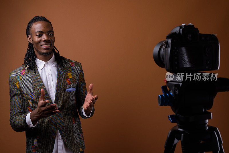 工作室拍摄的年轻英俊的非洲商人在彩色背景下的视频博客