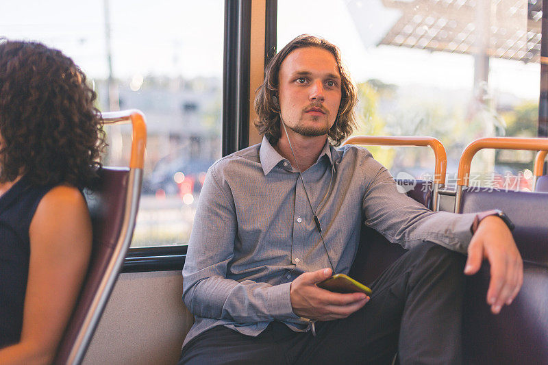 戴耳机乘坐公共交通工具和看手机的男人