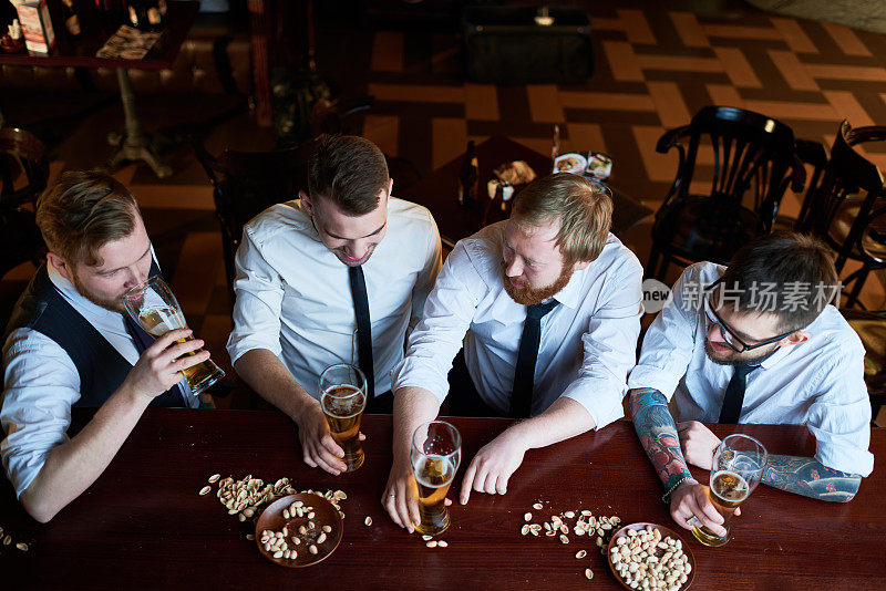 兴奋的朋友们穿着衬衫，打着领带，喝着啤酒，吃着开心果
