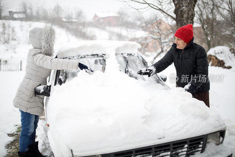 一位妇女正在清理一辆被雪覆盖的汽车。在大雪堆周围