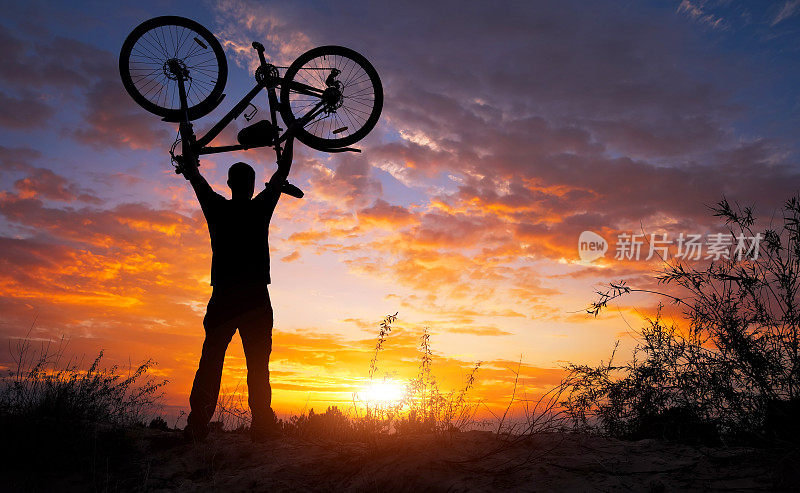 在夕阳西下的草地上，那个人把自行车举过头顶站着