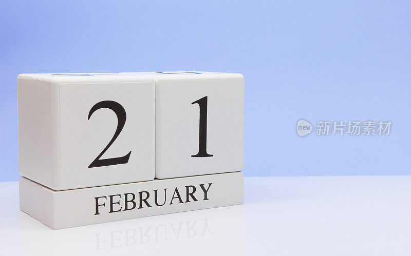 2月21日。月21日，日历在白色的桌子上反射，以浅蓝色为背景。冬天的时候，空白的文字