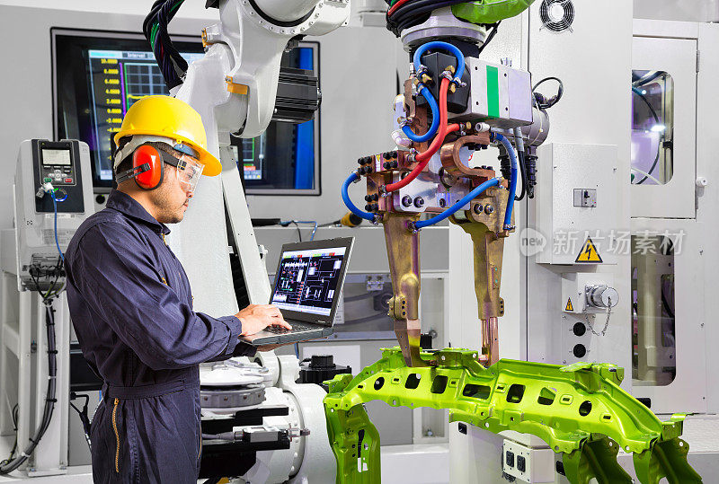 维护工程师使用笔记本电脑控制机器人抓取汽车工件在智能工厂，工业4.0的概念