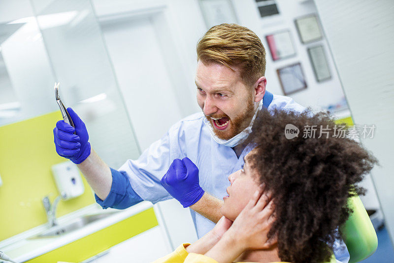 一名医生在一名痛苦的拔牙患者面前摆出一个庆祝的姿势，用医疗镊子夹着一颗拔出来的牙齿