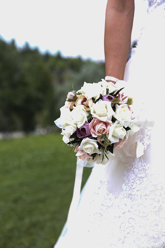 新娘手捧紫色和白色的婚礼花束。新娘捧花束