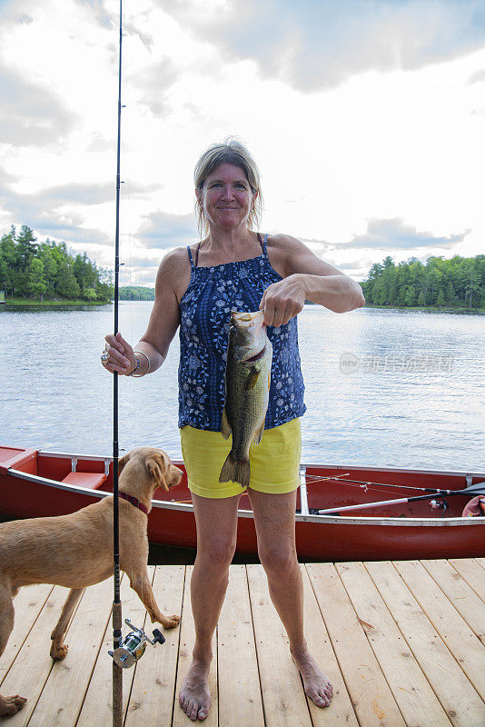 一个成熟的女人手里拿着一条刚在湖里钓到的大口鲈鱼。