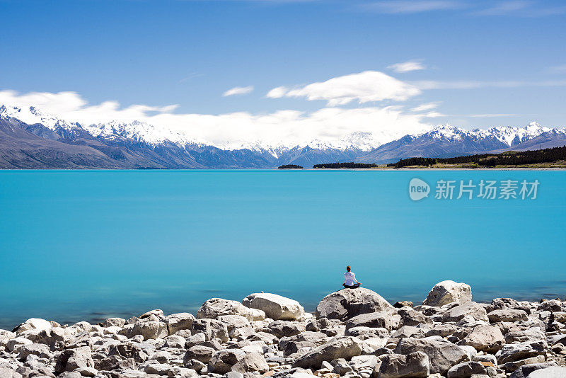 女性在面对普卡基湖和库克山的岩石上冥想，长时间暴露