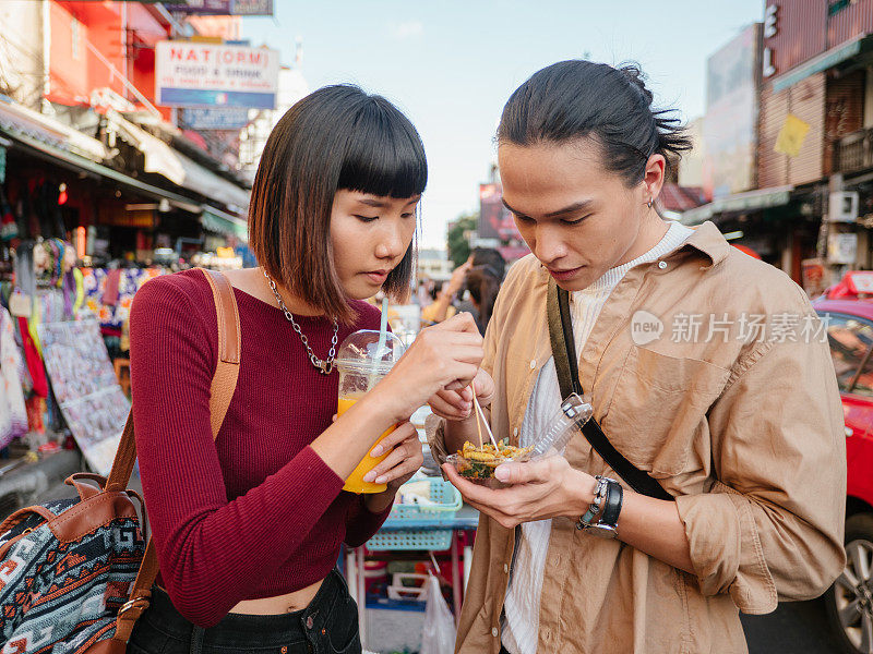 一对年轻的亚洲夫妇在曼谷考山路的一个街头食品市场购买炒昆虫