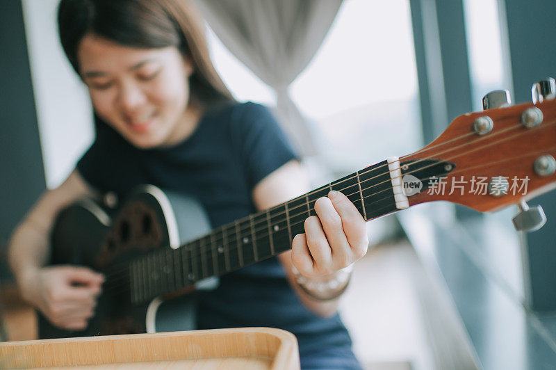 一位亚洲华人年轻女子在业余时间在家弹吉他，心情愉快