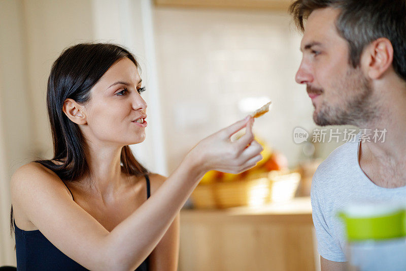 快乐的年轻女子给她的男朋友一块面包咬