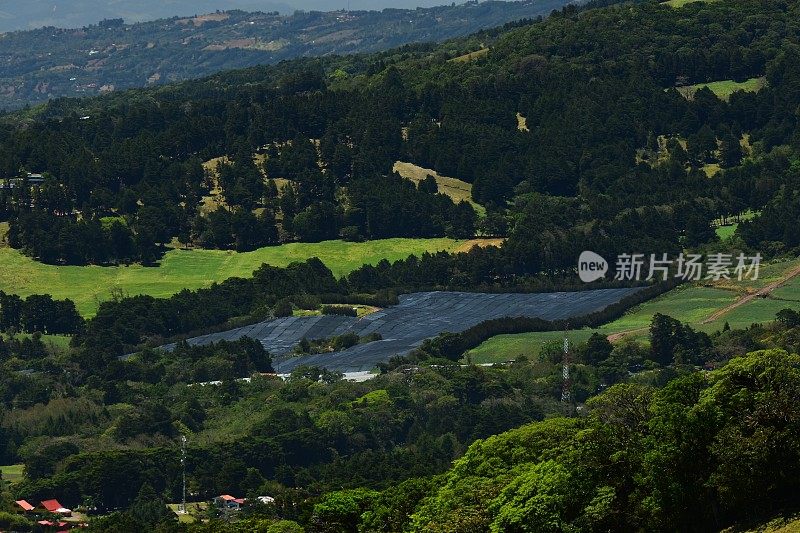 丘陵地带有小片的森林、田野和遮蔽农作物的深色遮荫布