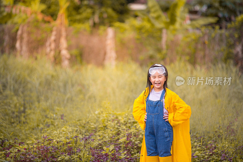 一个亚洲的中国女孩穿着雨衣和农家鞋在农场的草地上玩耍。