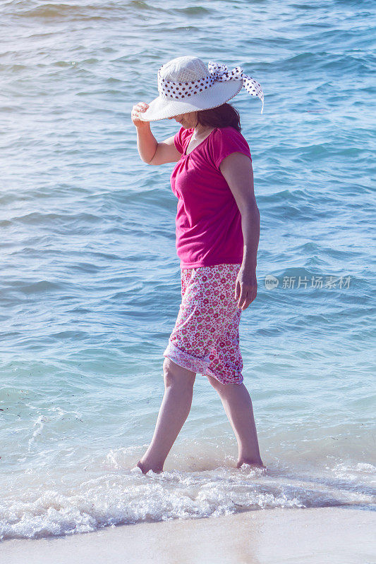 一个成年女子在海滩上散步，脚浸在海里