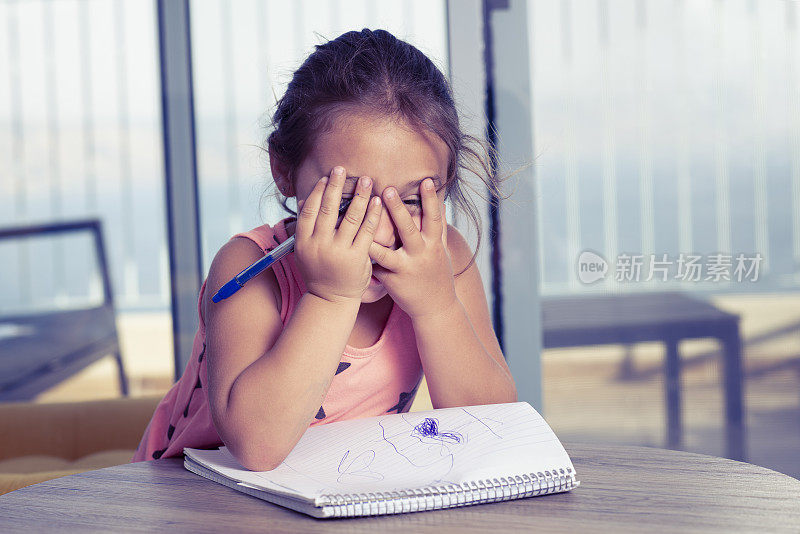 一个害羞的女孩用手捂着脸。写作阶段。儿童写作在家里的发展。