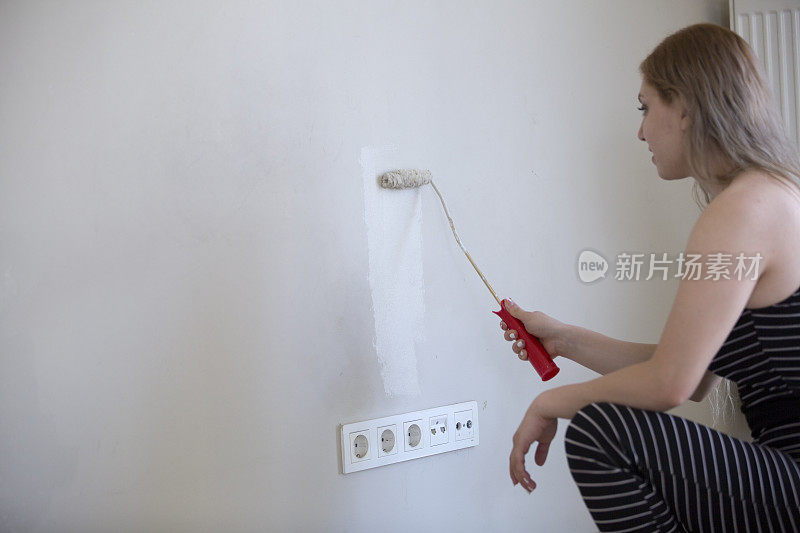 年轻女子正在用油漆滚筒和刷子刷墙